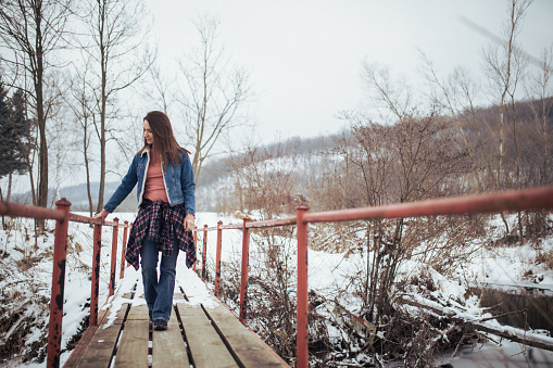 Young woman standing on the bridge in winter, rural scene.