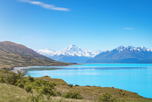 View towards the beautiful turquoise Lake Pukaki and snow capped Mount Cook Glacier Mountain Range in Summer. South Island, Canterbury, Mackenzie Basin, Mount Cook, Lake Pukaki, New Zealand