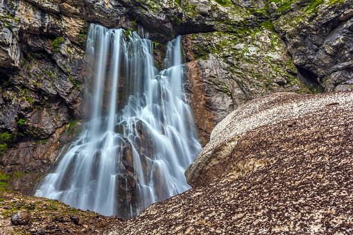 A large waterfall descending from the rocks and crashing against the stones, during the melting of the snow in the spring in rainy weather.
