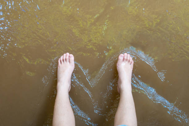 The boy put his foot on the surface of the river