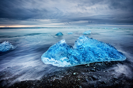 long exposure of the moving water over the black sand and iceberg in jokulsarlom lagoon