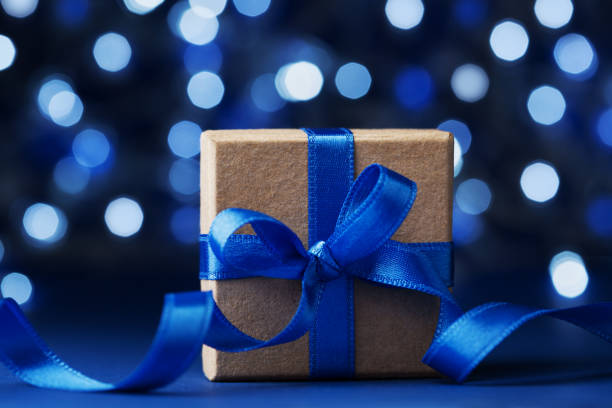 istock Christmas gift box or present with bow ribbon against blue bokeh background. Magic holiday greeting card. 861658586
