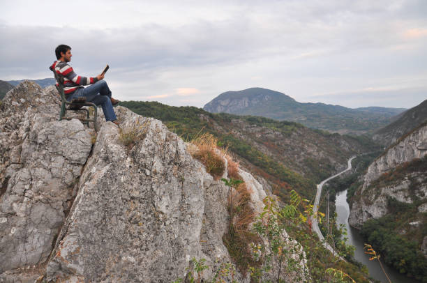 istock Man sitting and reading on the edge of a cliff surrounded by nature. 861677794