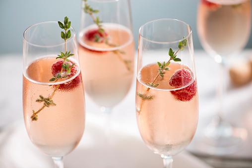 Flutes of pink rose champagne garnished with red raspberries and green thyme make for a festive cocktail gathering.