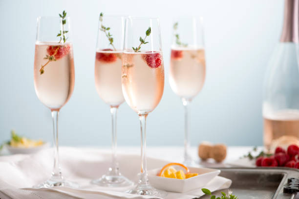 Rose Champagne Cocktails Flutes of pink rose champagne garnished with red raspberries and green thyme make for a festive cocktail gathering. carbonated stock pictures, royalty-free photos & images