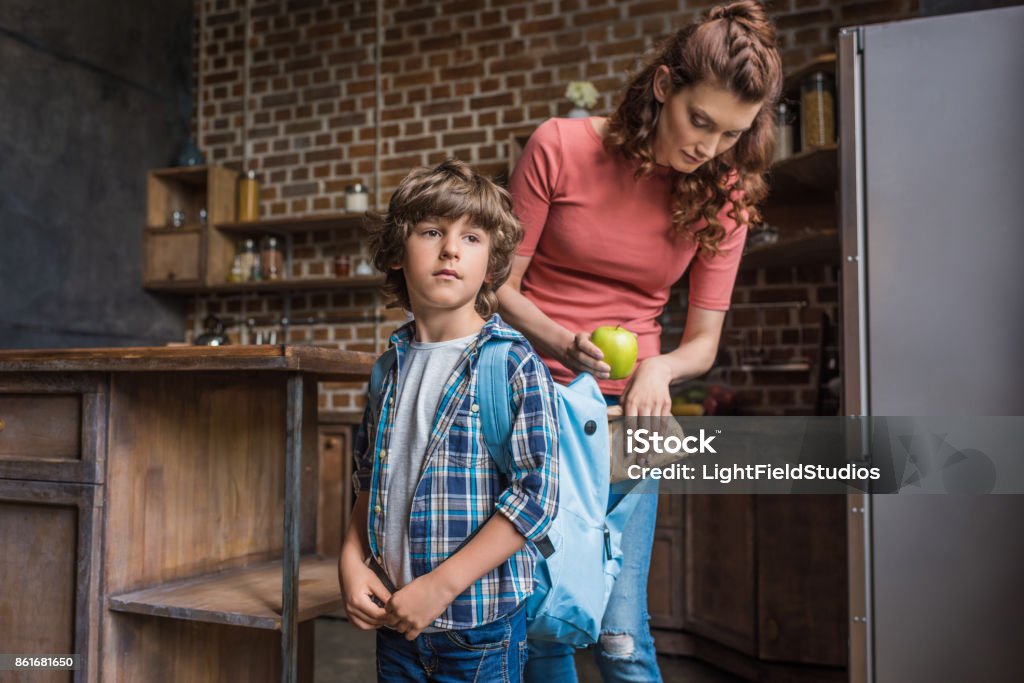 mother packing son before school mother putting lunch into sons backpack before school Packing Stock Photo