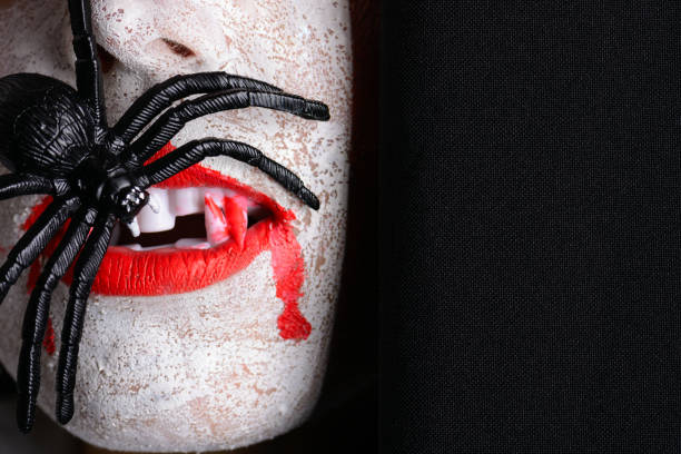 Scary fanged halloween vampire eating a spider A scary fanged halloween vampire with sharp red claws eating a spider against a black background. fanged stock pictures, royalty-free photos & images