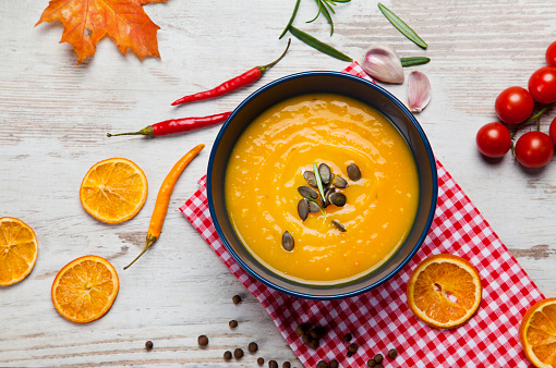 Bowl of pumpkin soup on rustic background with leaves and oranges