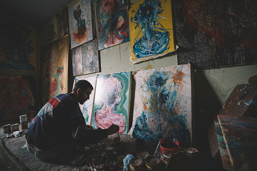 One man, painting in his home studio, paintings all around him.