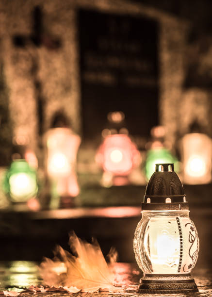 Sepulchral candle on the grave with some unfocused candles and tombstone in the background - vertical