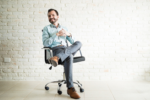 Attractive young freelancer sitting in an office chair and looking confident with a smile