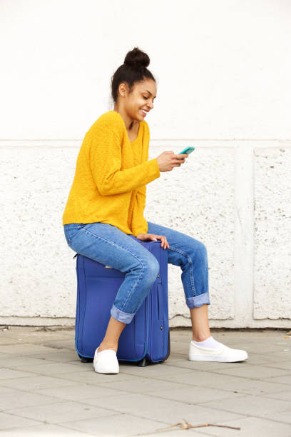 istock Cheerful woman using mobile phone and sitting on suitcase 861761524