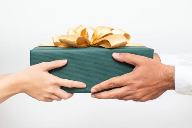 Couple holding packaged Christmas present together Close-up of couple holding packaged Christmas present together. Woman passing gift to boyfriend while congratulating him with New Year. Christmas gift-giving concept passing giving stock pictures, royalty-free photos & images