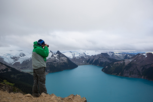 A young man on a hike uses his camera to take a picture of the beautiful landscape