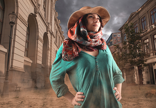 Explorer woman discovers unpopulated city . Beautiful woman wearing a cowboy hat and walking in a city covered by sand.