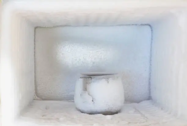 Stainless steel drinking water glass in freezer of a refrigerator. Ice buildup inside of a freezer walls.