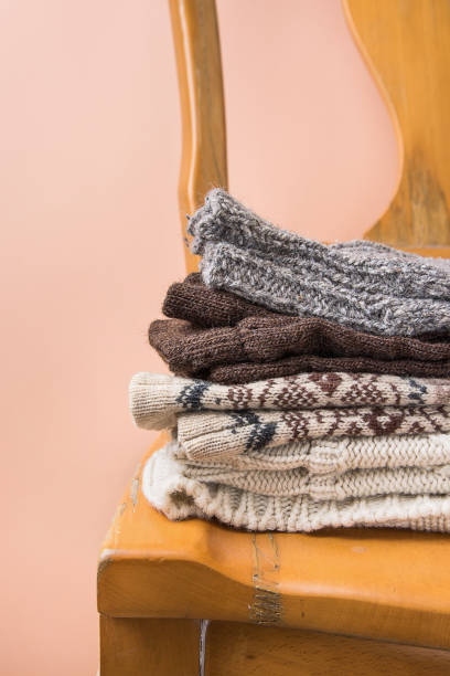 istock Stack of Handmade Warm Knitted Socks Scarfs Mittens Sweaters From Rough Wool Yarn Brown Beige Grey on Vintage Chair Trendy Peach Color Wall Background. Eco Fashion Kinfolk Style. Interior 861859042