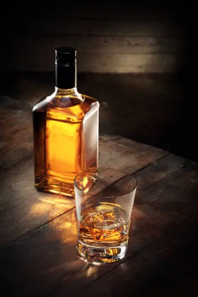 close up view of glass of  whiskey and a bottle aside on color background
