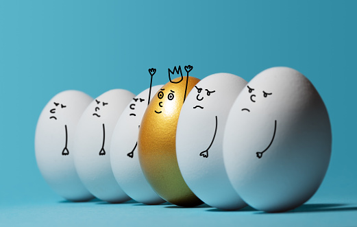 Concept of individuality, exclusivity, better choice and winning. A smiling golden egg with a crown among angry and sad white eggs on blue background. Eggs with funny drawn faces.