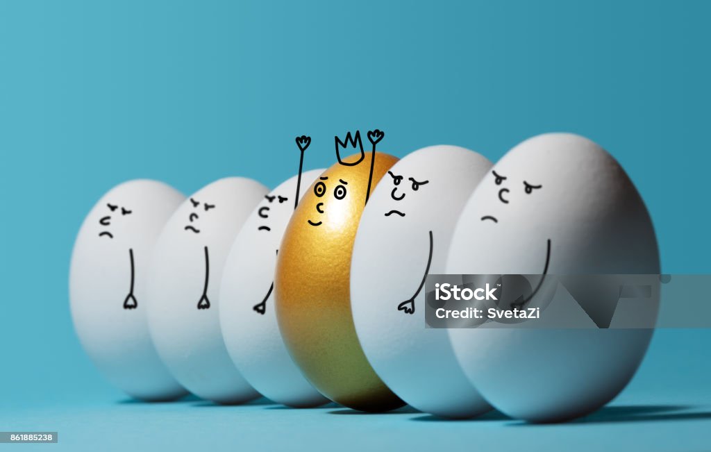 Concept of individuality, exclusivity, better choice and winning. Concept of individuality, exclusivity, better choice and winning. A smiling golden egg with a crown among angry and sad white eggs on blue background. Eggs with funny drawn faces. Standing Out From The Crowd Stock Photo