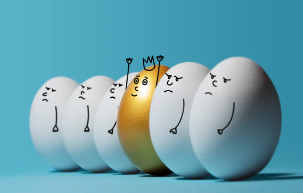 Concept of individuality, exclusivity, better choice and winning. Concept of individuality, exclusivity, better choice and winning. A smiling golden egg with a crown among angry and sad white eggs on blue background. Eggs with funny drawn faces. prosperity photos stock pictures, royalty-free photos & images