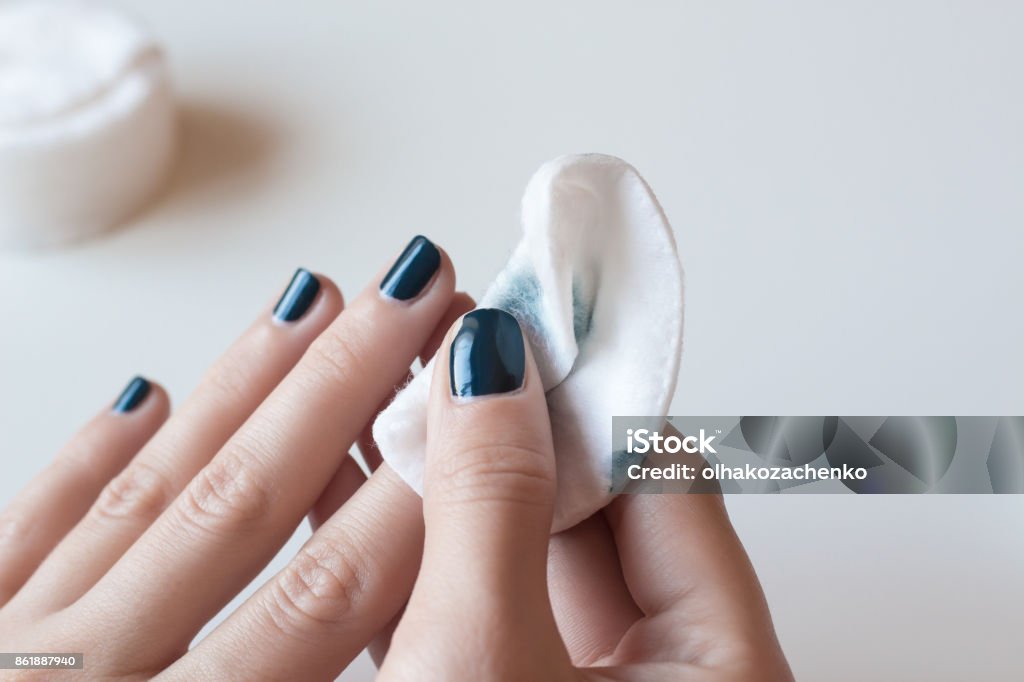 Woman removes the nail polish. Dark blue manicure. Woman removes the nail polish. Hands with dark blue manicure on whote table. Nail Polish Stock Photo