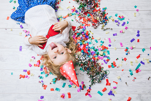 Little girl child cute and beautiful with multi-colored confetti on the floor and a festive hat happy happy bow