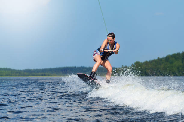 woman riding wakeboard on motorboat wave in lake