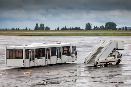 Shuttle bus and passenger boarding stairs at the airport apron in a rainy day