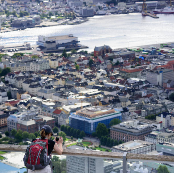 Woman enjoying the view from top of Mount Fløyen. Bergen city Bergen, Norway - August 9, 2017: Woman enjoying the view from top of Mount Fløyen taking picture. Bergen city including seen in background. Cruising ships in port. fløyen stock pictures, royalty-free photos & images