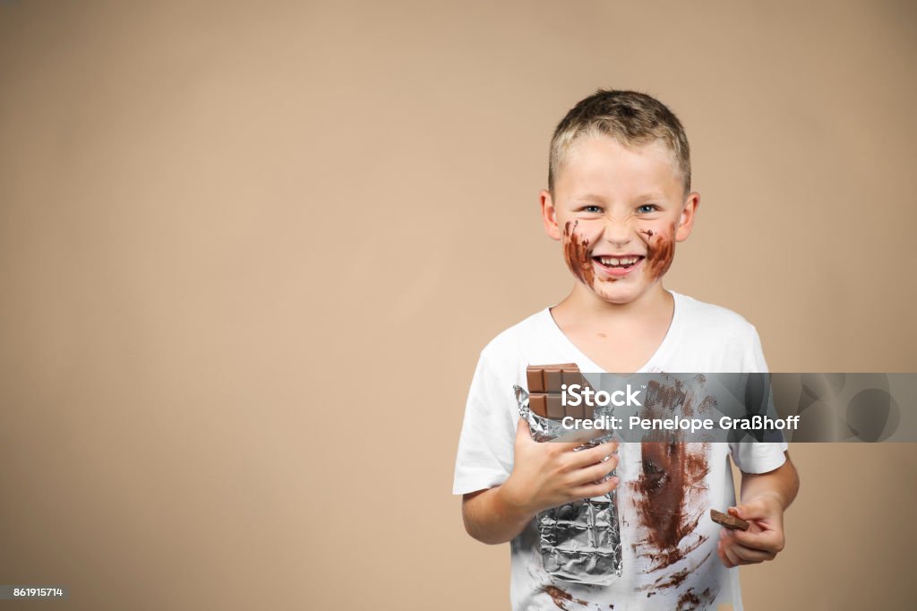 Little boy holds a bar of chocolate in his hand Little boy holds a bar of chocolate in his grin and has smudged clothes, against colored background Chocolate Stock Photo