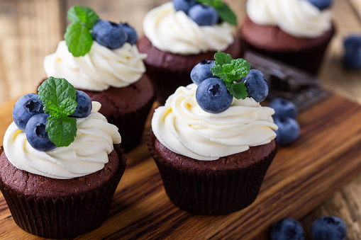 Blueberry and cream cheese  chocolate cupcakes on wooden board. Homemade summer dessert on  rustic table