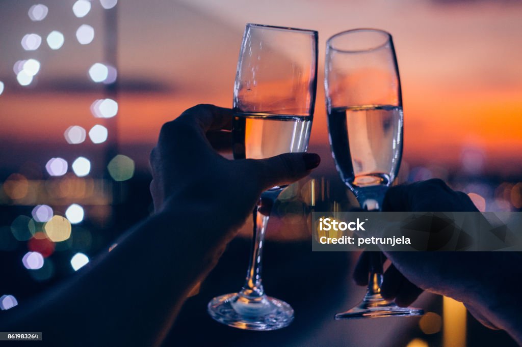 Drink for us Hands holding glasses of champagne , city in sunset in background Celebratory Toast Stock Photo