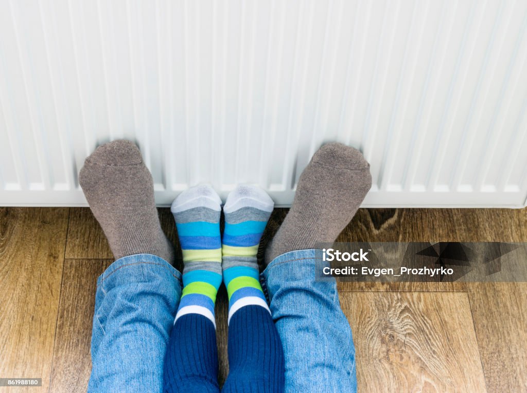 A man and a child in winter socks warm their feet near the heater. Radiator - Heater Stock Photo