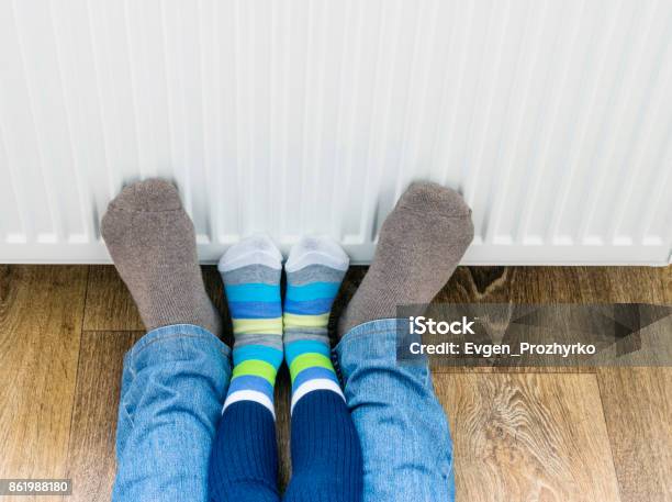 A Man And A Child In Winter Socks Warm Their Feet Near The Heater Stock Photo - Download Image Now
