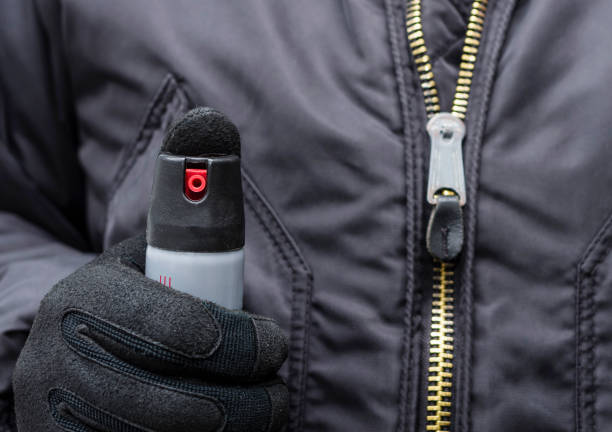 un hombre en negro táctico uniformes y guantes tiene un gas lacrimógeno o pimienta spray. medios de autodefensa. - pulverizador de pimienta fotografías e imágenes de stock