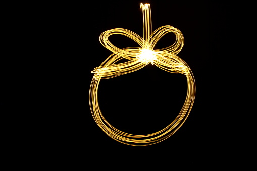 A long exposure photograph of gold fairy lights in a round Christmas ornament shape pattern, against a clean black background