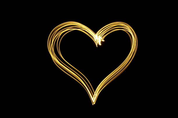 A long exposure photograph of gold fairy lights in a heart shape against a clean black background