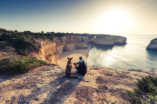 Best friends travellers sitting at cliffs in Portugal at sunset.