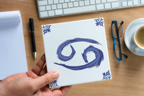 cancer  Delfts Blue zodiac tile above working desk Person holding Delfts Blue cancer  zodiac tile above working desk. Drawing on white tile by contributor cancer astrology sign photos stock pictures, royalty-free photos & images