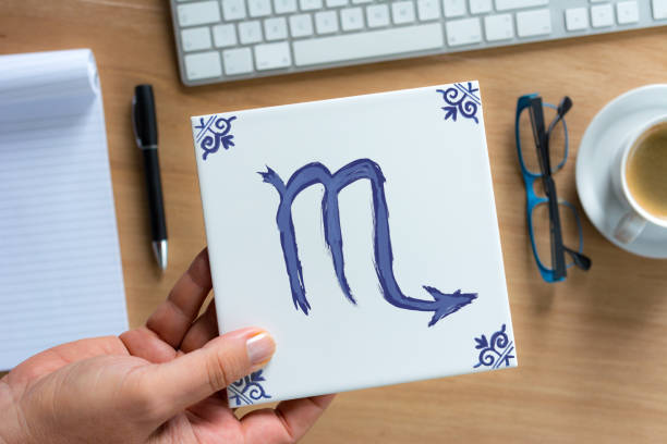 Person holding Delfts Blue scorpio zodiac tile above working desk. Drawing on white tile by contributor