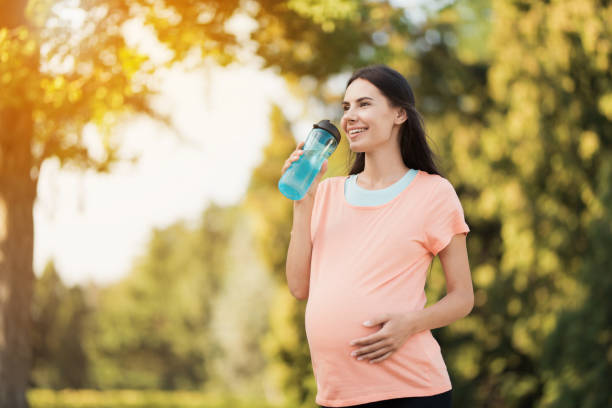pregnant woman walking in the park with a sports bottle in hands. she drinks from a bottle - child women outdoors mother imagens e fotografias de stock