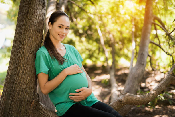 pregnant woman posing by a tree in the park - human pregnancy outdoors women nature imagens e fotografias de stock
