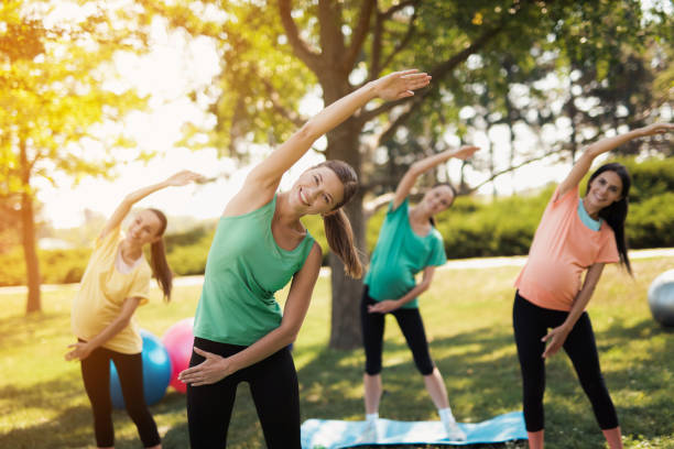 pregnancy yoga. three pregnant women standing in the park and doing exercises. together with them their coach - child women outdoors mother imagens e fotografias de stock