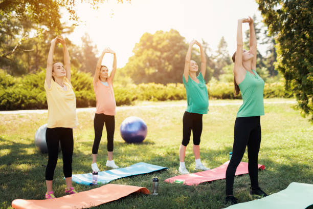 pregnancy yoga. three pregnant women standing in the park and doing exercises. together with them their coach - child women outdoors mother imagens e fotografias de stock