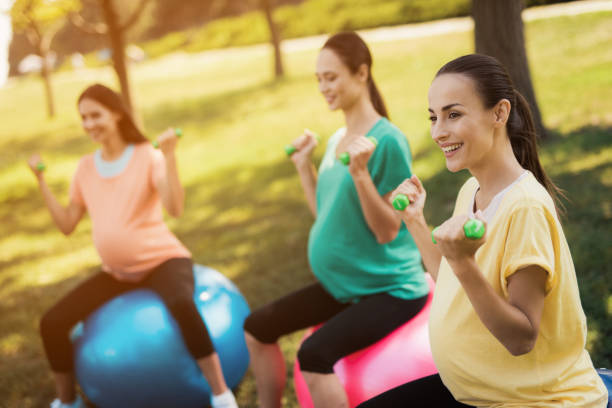pregnancy yoga. three pregnant women are engaged in fitness in the park. they sit on balls for yoga - human pregnancy outdoors women nature imagens e fotografias de stock