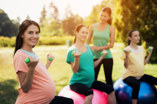 Pregnancy yoga. Three pregnant women are engaged in fitness in the park. They sit on balls for yoga Pregnancy yoga. Three pregnant women are engaged in fitness in the park. They sit on balls for yoga. With them their coach. They train with dumbbells crossfit girl stock pictures, royalty-free photos & images