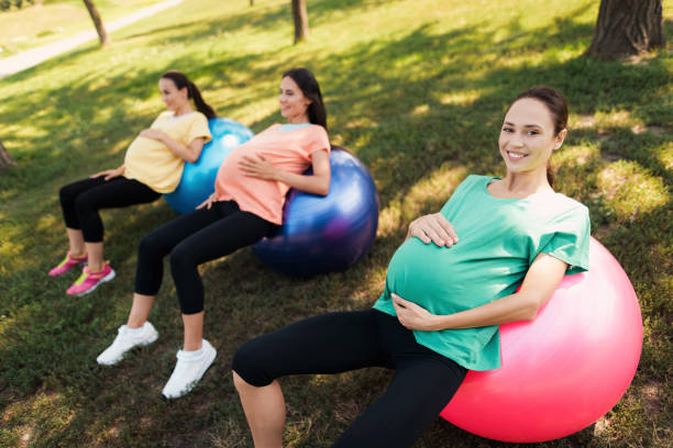 three pregnant women lie on yoga balls in the park. they holding their bellies - human pregnancy outdoors women nature imagens e fotografias de stock