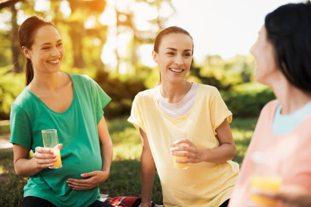 three pregnant women sit in the park after practicing yoga and drink juice. they are resting - child women outdoors mother imagens e fotografias de stock