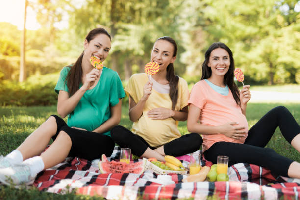 three pregnant women posing in a picnic park with large colored candies - human pregnancy outdoors women nature imagens e fotografias de stock